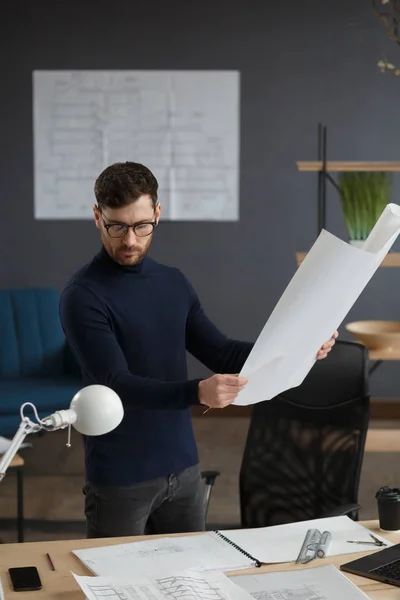 Arquitecto trabajando en la oficina con planos. Ingeniero inspeccionar plan arquitectónico, bosquejando un proyecto de construcción. Retrato de hombre barbudo guapo sentado en el lugar de trabajo. Concepto de construcción empresarial — Foto de Stock