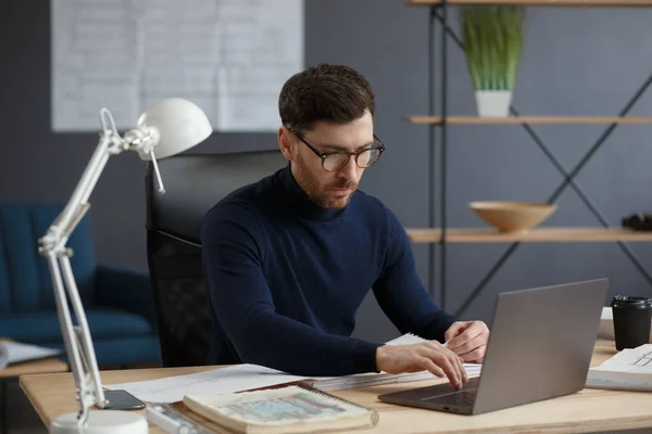 Arquitecto trabajando en oficina con laptop. Ingeniero piensa en el plan arquitectónico, la búsqueda de nuevas ideas para el proyecto de construcción. Retrato del guapo barbudo sentado en el lugar de trabajo. Concepto empresarial —  Fotos de Stock