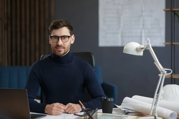 Arquitecto trabajando en oficina con laptop. Retrato de negocios de un hombre barbudo guapo con anteojos sentados en el trabajo. Un hombre de negocios seguro tuvo éxito. Concepto empresarial —  Fotos de Stock