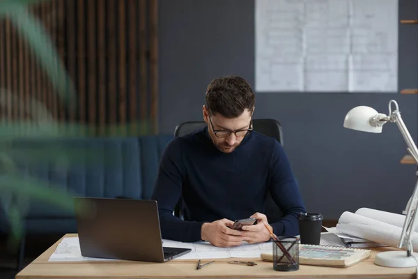 Arquitecto trabajando en la oficina con planos. Ingeniero inspeccionar plan arquitectónico, bosquejando un proyecto de construcción. Retrato de hombre barbudo guapo sentado en el lugar de trabajo. Concepto de construcción empresarial —  Fotos de Stock