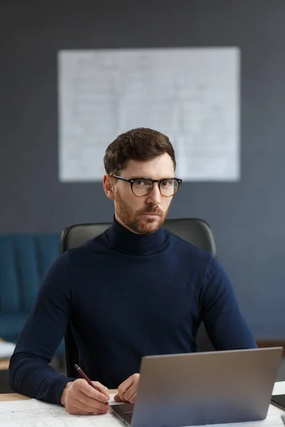 Молодой бизнесмен работает в офисе с ноутбуком. Деловой портрет красивого бородатого мужчины в очках, сидящего на рабочем месте. Уверенный бизнесмен стал успешным. Концепция бизнеса — стоковое фото