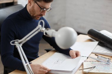 Ofiste planlarla çalışan bir mimar. Mühendis mimari planı inceliyor, bir inşaat projesi çiziyor. İş yerinde oturan sakallı yakışıklı bir adamın portresi. İş inşa kavramı