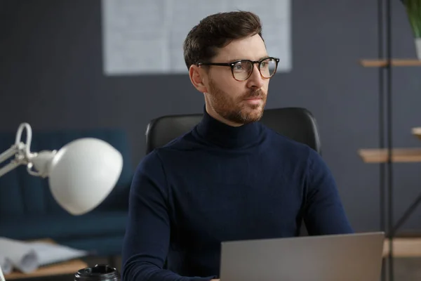 Архитектор работает в офисе с ноутбуком. Деловой портрет красивого бородатого мужчины в очках, сидящего на рабочем месте. Уверенный бизнесмен стал успешным. Концепция бизнеса — стоковое фото