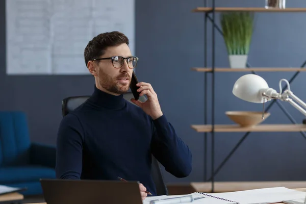 Építész beszél telefonon az irodában. A magabiztos üzletember üzleti partnerekkel tárgyal. Üzleti portré egy jóképű szakállas férfiról, aki szemüvegben ül a munkahelyén. Üzleti koncepció — Stock Fotó