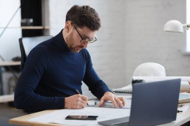 Ofiste planlarla çalışan bir mimar. Mühendis mimari planı inceliyor, bir inşaat projesi çiziyor. İş yerinde oturan sakallı yakışıklı bir adamın portresi. İş inşa kavramı