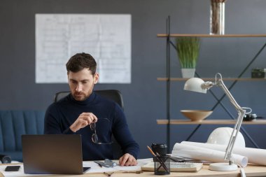 Ofiste dizüstü bilgisayarla çalışan bir mimar. Mühendis mimari plan üzerinde düşünüyor, inşaat projesi için yeni fikirler arıyor. İş yerinde oturan yakışıklı sakallı adamın portresi. İş konsepti