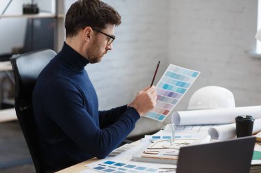 Ofiste renk paletiyle çalışan bir mimar. Mühendis renk örnekleri kullanarak bina için renkler seçiyor, inşaat projesi için yeni fikirler arıyor. İş yerinde sakallı yakışıklı bir adamın portresi.