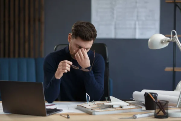 Arquitecto cansado trabajando horas extras en la oficina. Los empresarios estresados tienen problemas financieros y buscan ideas para superar la crisis financiera. Empresario en bancarrota. Concepto de agotamiento y exceso de trabajo —  Fotos de Stock