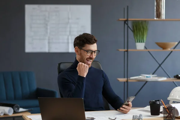 Joven usando smartphone y sonriendo. Feliz hombre de negocios utilizando aplicaciones de teléfono móvil, mensaje de texto, navegación por Internet, mirando el teléfono inteligente. Concepto de jóvenes que trabajan con dispositivos móviles — Foto de Stock