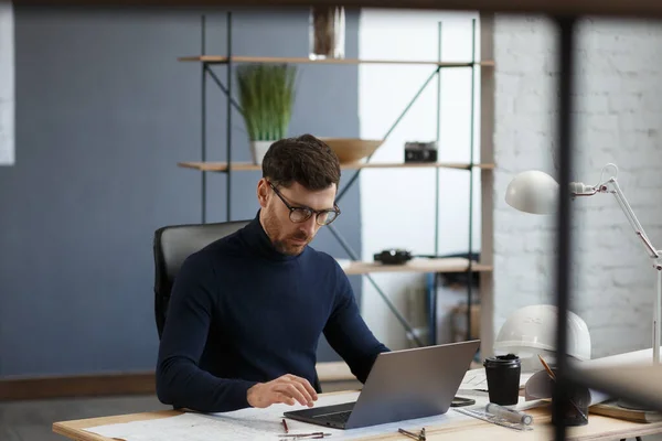 Arquitecto trabajando en la oficina con planos. Ingeniero inspeccionar plan arquitectónico, bosquejando un proyecto de construcción. Retrato de hombre barbudo guapo sentado en el lugar de trabajo. Concepto de construcción empresarial — Foto de Stock