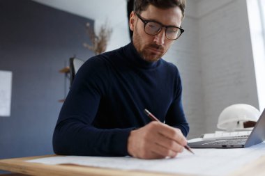 Ofiste planlarla çalışan bir mimar. Mühendis mimari planı inceliyor, bir inşaat projesi çiziyor. İş yerinde oturan sakallı yakışıklı bir adamın portresi. İş inşa kavramı