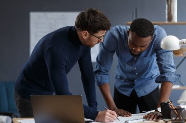 Çok ırklı mühendis ekibi mavi baskılar ve mimar ekipmanlarıyla birlikte çalışıyor, taslak çiziyorlar, tartışıyorlar ve inşaat projesini planlıyorlar. Ortaklar iş yerinde tartışır. İş inşa kavramı