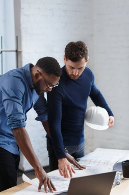 Çok ırklı mühendis ekibi mavi baskılar ve mimar ekipmanlarıyla birlikte çalışıyor, taslak çiziyorlar, tartışıyorlar ve inşaat projesini planlıyorlar. Ortaklar iş yerinde tartışır. İş inşa kavramı