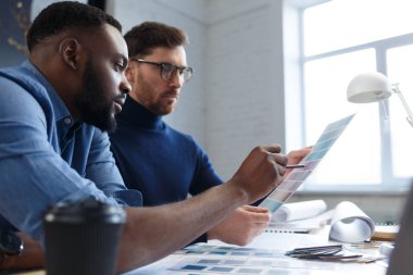 Renk paletinde çalışan çok ırklı mühendis takımı. Mimarlar bina renklerini renk örnekleri, çizim ve inşaat projeleri kullanarak seçerler. İş yerinde tartışan ortaklar