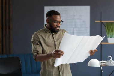 Ofiste projelerle çalışan Afro-Amerikalı bir mimar. Mühendis mimari planı inceliyor, bir inşaat projesi çiziyor. İş yerinde oturan siyah yakışıklı adamın portresi. İş konsepti