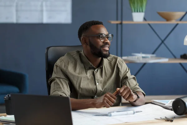 Arquitecto afro-americano que trabaja en oficina con planos. Ingeniero inspecciona plano arquitectónico, dibujando un proyecto de construcción. Retrato de un hombre guapo negro sentado en el lugar de trabajo. Concepto empresarial — Foto de Stock