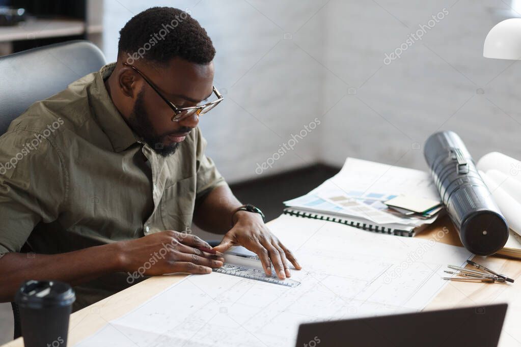 Afro-American architect working in office with blueprints.Engineer inspect architectural plan, sketching a construction project. Portrait of black handsome man sitting at workplace. Business concept