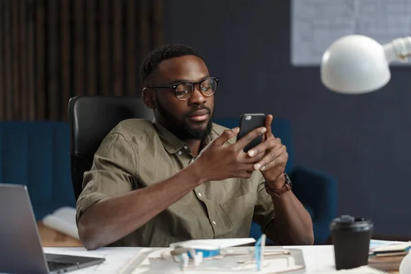 Fiatal afro-amerikai férfi okostelefonnal és mosollyal. Boldog üzletember, aki mobiltelefonos alkalmazásokat használ, SMS-t ír, internetezik, okostelefont néz. Mobil eszközökkel dolgozó fiatalok — Stock Fotó