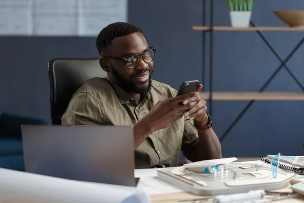 Ung afro-amerikansk man som använder smartphone och ler. Glad affärsman som använder mobilappar, sms, surfar på internet, tittar på smartphone. Ungdomar som arbetar med mobila enheter — Stockfoto