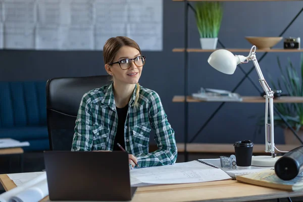 Diseñadora de interiores femenina trabajando en oficina con laptop. Arquitecto reflexiona sobre el plan arquitectónico, buscando nuevas ideas para el proyecto de construcción. Mujer sentada en el lugar de trabajo. Concepto de retrato empresarial —  Fotos de Stock