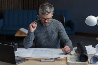 Ofiste planlarla çalışan iç mimar. Mühendis mimari planı inceliyor, bir inşaat projesi çiziyor. İş yerinde sakallı yakışıklı bir adamın portresi. İş inşa kavramı