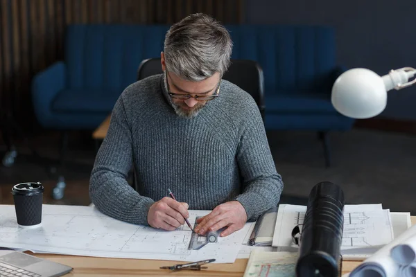 Diseñador de interiores que trabaja en la oficina con planos. Ingeniero inspeccionar plan arquitectónico, bosquejando un proyecto de construcción. Retrato de hombre barbudo guapo en el lugar de trabajo. Concepto de construcción empresarial — Foto de Stock