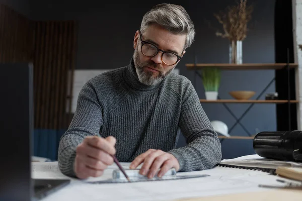 Interieurontwerper werkt in het kantoor met blauwdrukken. Ingenieur inspecteert architectonisch plan, schetsen van een bouwproject.Portret van knappe bebaarde man op het werk. Bedrijfsbouwconcept — Stockfoto