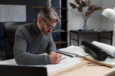 Mimar ofiste planlar çiziyor. Mühendis bir inşaat projesi çiziyor. Mimari plan. Yakışıklı sakallı adamın işine odaklanmış yakın plan portresi. İş inşa kavramı