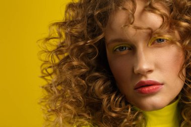 Close up fashion studio portrait of young beautiful women with curly hair.Nice girl with wavy hairstyle and bright make up isolated over yellow background.Beauty and hair care concept.Yellow lifestyle