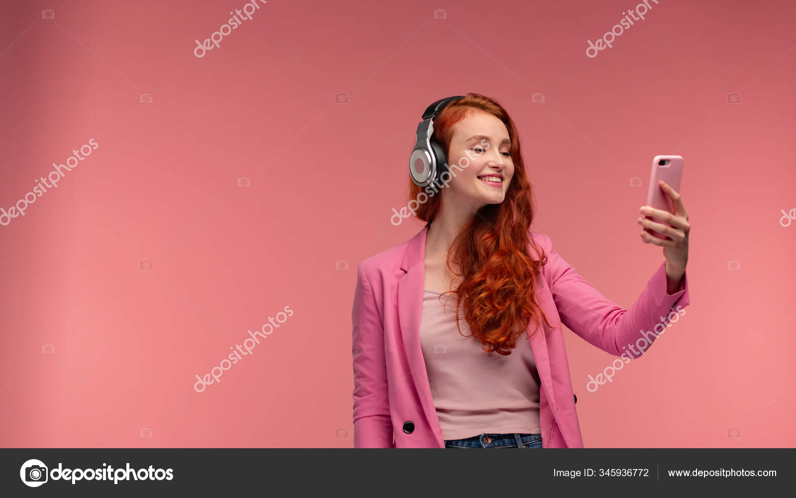 Enjoy listening to music. Beautiful young redhead woman with headphones listening music on smart phone using music app. Funny smiling girl with earphones and mobile phone on pink background Stock Photo by © Enjoy listening to music. Beautiful young redhead woman with headphones listening music on smart phone using music app. Funny smiling girl with earphones and mobile phone on pink background Stock Photo by ©