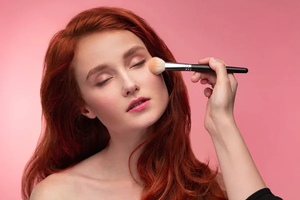 Makeupartist applicerar puder. Hand make-up mästare, måla kinder av ung rödhårig flicka. Porträtt av vacker frisk flicka med ren ren hud och naturlig make-up. Skönhetsbegreppet — Stockfoto