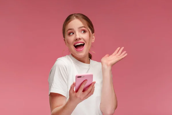 The best day ever. Surpised young redhead woman holding pink smartphone, smiling and expressing positivity. Happy girl got shocking positive news. Copy space. Young people working with mobile devices. — Stock Photo, Image