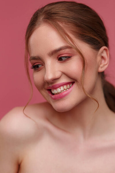 Beauty portrait of smiling redhead girl. Perfect skin. Beautiful female model with long hair over pink background. Young cute woman with clear skin. Skincare and facial treatment concept
