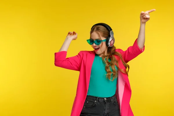 Desfrute de ouvir música. Mulher ruiva jovem em fones de ouvido ouvir música. Menina sorrindo engraçado em fones de ouvido e jaqueta rosa dançando e cantando em fundo amarelo. Relaxamento e gestão do stress — Fotografia de Stock