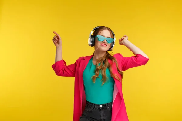 Desfrute de ouvir música. Mulher ruiva jovem em fones de ouvido ouvir música. Menina sorrindo engraçado em fones de ouvido e jaqueta rosa dançando e cantando em fundo amarelo. Relaxamento e gestão do stress — Fotografia de Stock