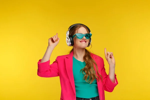 Desfrute de ouvir música. Mulher ruiva jovem em fones de ouvido ouvir música. Menina sorrindo engraçado em fones de ouvido e jaqueta rosa dançando e cantando em fundo amarelo. Relaxamento e gestão do stress — Fotografia de Stock