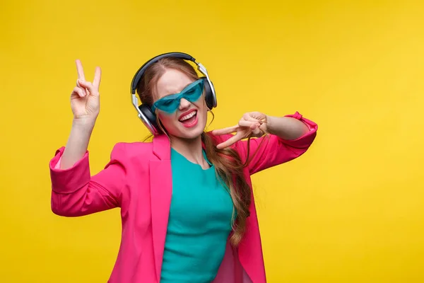 Desfrute de ouvir música. Mulher ruiva jovem em fones de ouvido ouvir música. Menina sorrindo engraçado em fones de ouvido e jaqueta rosa dançando e cantando em fundo amarelo. Relaxamento e gestão do stress — Fotografia de Stock