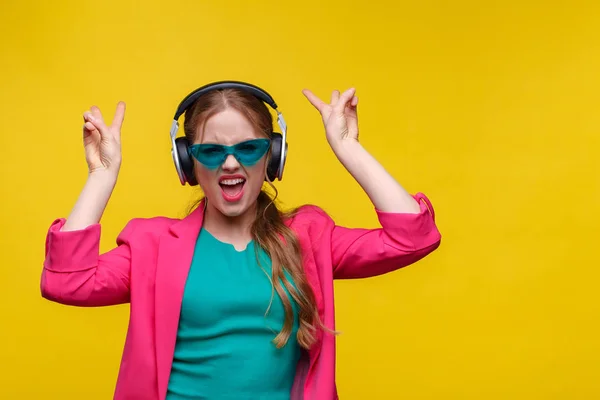 Desfrute de ouvir música. Mulher ruiva jovem em fones de ouvido ouvir música. Menina sorrindo engraçado em fones de ouvido e jaqueta rosa dançando e cantando em fundo amarelo. Relaxamento e gestão do stress — Fotografia de Stock