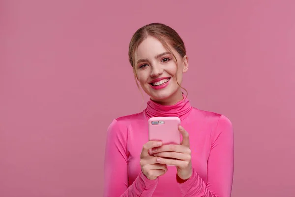 Funny young redhead woman holding pink smartphone and smiling.Happy girl using mobile phone apps, texting message, browsing internet, looking at smartphone. Young people working with mobile devices — Stock Photo, Image