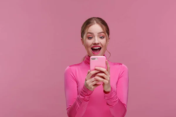 The best day ever. Surpised young redhead woman holding pink smartphone, smiling and expressing positivity. Happy girl got shocking positive news. Copy space. Young people working with mobile devices — Stock Photo, Image