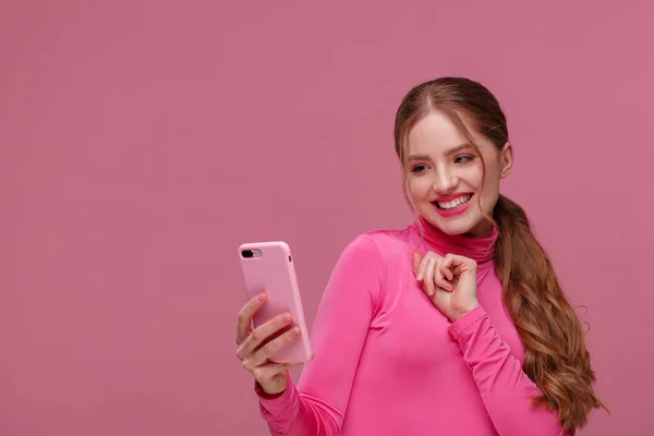 Funny young redhead woman holding pink smartphone and smiling.Happy girl using mobile phone apps, texting message, browsing internet, looking at smartphone. Young people working with mobile devices — Stock Photo, Image
