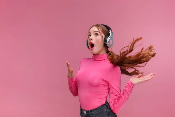 Disfruta escuchando música. Hermosa joven pelirroja en auriculares escuchando música. Chica sonriente divertida en auriculares y blusa rosa bailando sobre fondo rosa. Relajación y manejo del estrés. —  Fotos de Stock