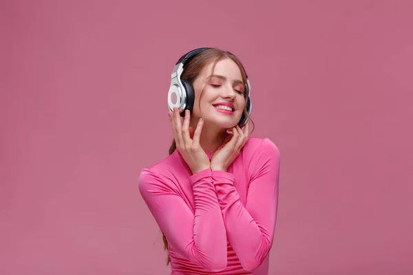 Disfruta escuchando música. Hermosa joven pelirroja en auriculares escuchando música. Chica sonriente divertida en auriculares y blusa rosa bailando sobre fondo rosa. Relajación y manejo del estrés —  Fotos de Stock
