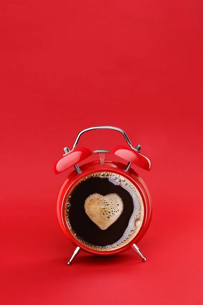 Morning coffee preparing witk love. Coffee time concept. Coffee break. Vintage red twin bell alarm clock with cup of coffee and cream heart isolated on red background. Copy space