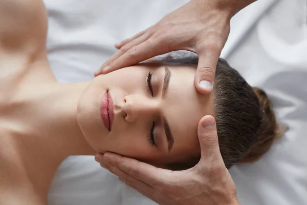 Joven hermosa mujer disfrutando de anti-envejecimiento masaje.Male facial terapeuta haciendo masaje de cabeza a la client.Professional femenina masseur.Relaxation, belleza, spa, cuerpo y rostro concepto de tratamiento — Foto de Stock