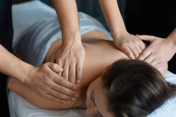 Молода красива жінка насолоджується масажем спини та плечей у спа-салоні. Професійний масажист лікує пацієнта жінки в квартирі.Релаксація, краса, концепція лікування тіла та обличчя. Домашній масаж — стокове фото