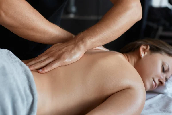 Ung vacker kvinna njuter av rygg och shouders massage i spa.Professionell massage terapeut behandlar en kvinnlig patient i lägenhet.Avkoppling, skönhet, kropp och ansikte behandlingskoncept.Hem massage — Stockfoto