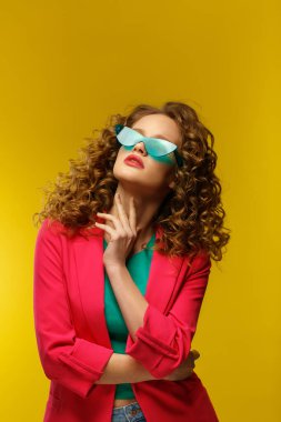 Kıvırcık saçlı güzel kadınların moda stüdyosu portresi. Dalgalı saçlı, parlak makyajlı ve sarı arka planda izole edilmiş gözlüklü hoş bir kız. Güzellik ve saç bakımı konsepti.