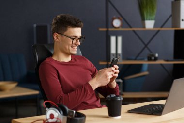 Genç adam akıllı telefon kullanıyor ve gülümsüyor. Mutlu iş adamı