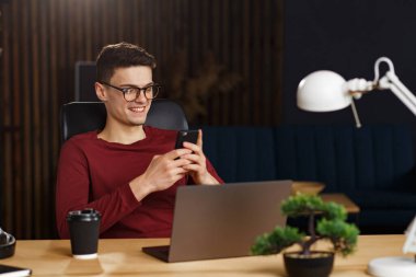 Genç adam akıllı telefon kullanıyor ve gülümsüyor. Mutlu iş adamı